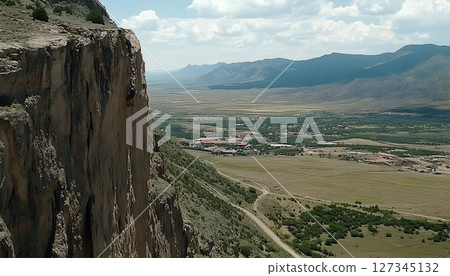 A daring solo climber ascending a sheer cliff face with expansive valley view 127345132