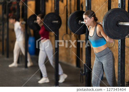 Slender girl trains muscles of arms and back using barbell and differentiated weighting in gym Slender girl trains muscles of arms and back using barbell and differentiated weighting in gym 127345404