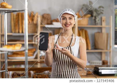 Portrait of female baker with mobile phone in hands in bakery interior 127345406