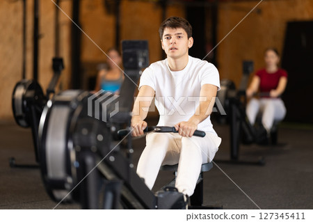 Focused guy works out with rowing machine during class at fitness club 127345411