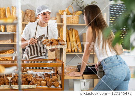 In bakery, girl client communicates with guy seller, asks about buns, 127345472