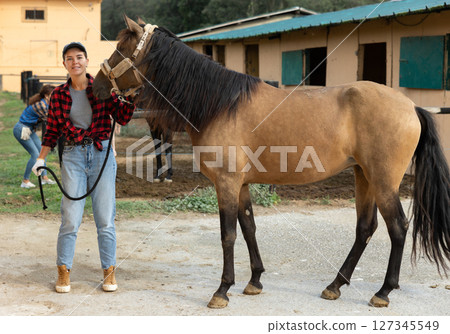 Portrait of female owner of horse farm shows her farm against backdrop of corral for walking horses 127345549
