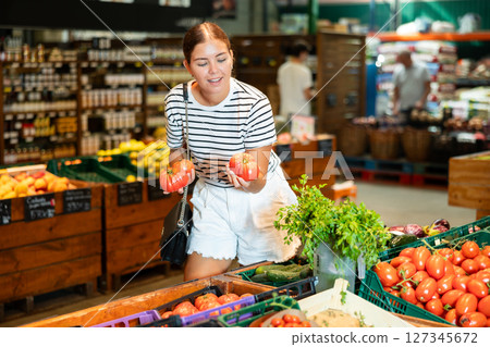 Young female shopper looking for fresh ripe tomatoes in supermarket Young female shopper looking for fresh ripe tomatoes in supermarket 127345672