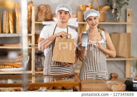 Young woman and guy sellers with bag and smartphone in bakery Young woman and guy sellers with bag and smartphone in bakery 127345689
