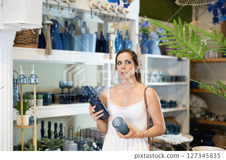 Woman examining decorative blue glass items in home decor store 127345835