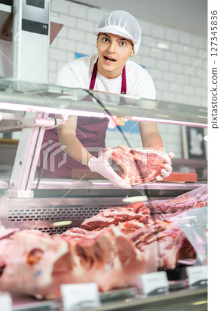 Positive young salesman demonstrating piece of meat in butcher shop 127345836