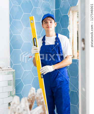Portrait of builder man in blue overalls with building level in his hands 127346001