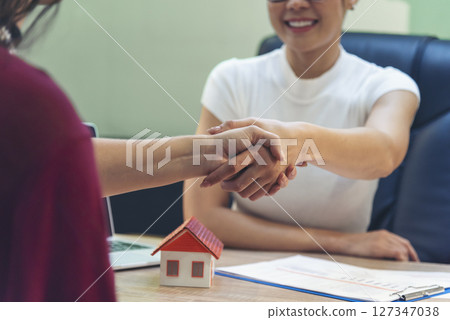 Close up Diversity women agent hands office desk. Crop Women handshake sign on insurance mortgage sale document. Businesswoman shakes hands customer dealing real estate house agent signing contract 127347038