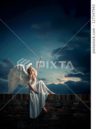 A fallen angel reaching his hands towards the heavens under the pre-dawn sky 127347943