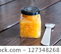 A glass jar and spoon filled with marmalade jam, made by sweetly stewing citrus peels and fruits. 127348268