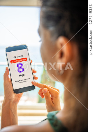 Young woman checking UV index on smartphone with high radiation alert. Mobile app warns to apply sunscreen before going outdoors 127349388