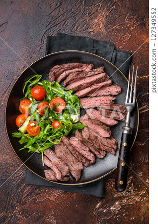 Grilled and sliced Beef Denver strip Steak on a plate with salad. brown background. top view 127349552