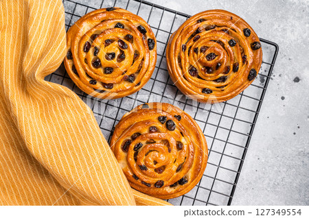 Baked Danish pastry, raisin bun on steel rack. grey background. top view Baked Danish pastry, raisin bun on steel rack. grey background. top view 127349554