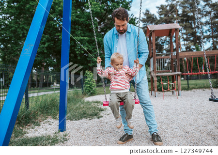 Father swinging small son on playground swing. 127349744