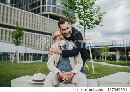 Father and adult son sitting on bench in park, sharing peaceful moment. 127349764