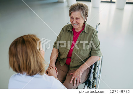 Senior woman in wheelchair smiling during conversation with caregiver. 127349785