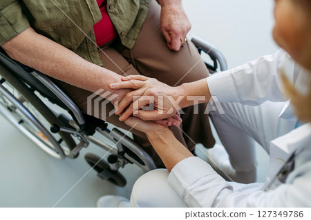 Nurse holding hands with elderly woman in wheelchair during comforting talk. Nurse holding hands with elderly woman in wheelchair during comforting talk. 127349786