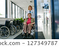 Geriatric doctor pushing a patient in a wheelchair down a hospital hallway. 127349787