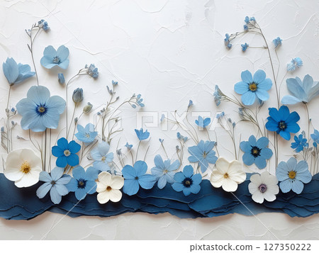 A serene arrangement of dried flowers in varying shades of blue and white, layered against a textured white background. 127350222