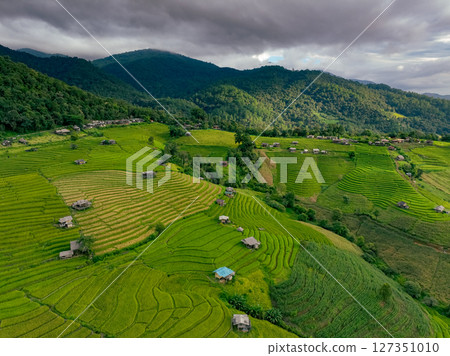 Aerial view of rice terraces with rich green hues and symmetrical patterns surrounded by remote farmland and rustic homestays. Eco travel and traditional countryside lifestyle. Mountain landscape. 127351010