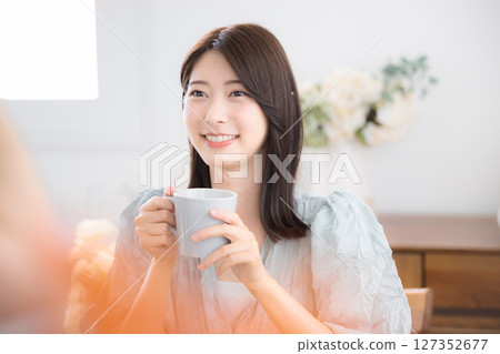 Cute young woman relaxing with a drink in her room, leisurely tea time 127352677