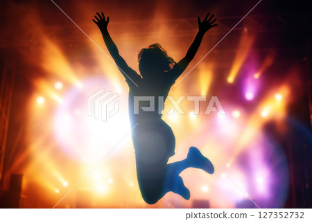 Silhouette of ecstatic woman jumping with arms up in front of bright stage lights during live music festival or concert Silhouette of ecstatic woman jumping with arms up in front of bright stage lights during live music festival or concert 127352732