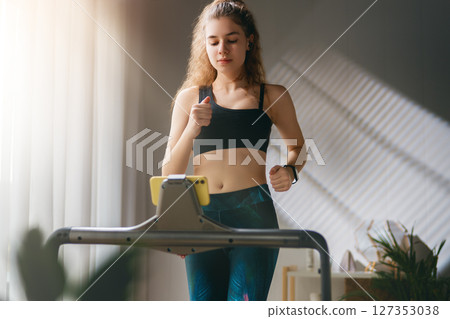 Young woman running on a treadmill indoors Young woman running on a treadmill indoors 127353038