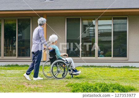 Senior couple in wheelchairs walking in front of their house Senior couple in wheelchairs walking in front of their house 127353977