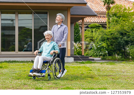 Senior couple in wheelchairs walking in front of their house 127353979