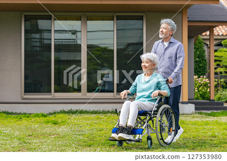 Senior couple in wheelchairs walking in front of their house 127353980