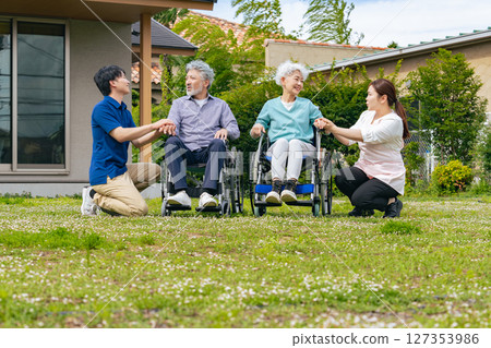 A senior couple in wheelchairs and a care staff member having a conversation in the garden 127353986