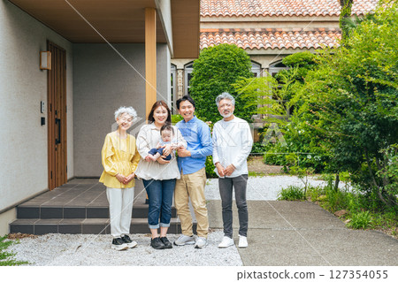 A three-generation family smiling and surrounding a baby in front of their house 127354055