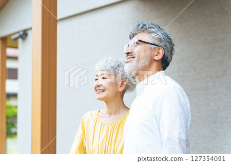Smiling senior couple standing in front of their house 127354091