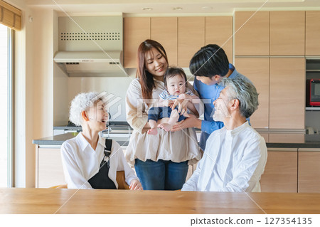 A group photo of a three-generation family happily gathered around a baby in a room 127354135
