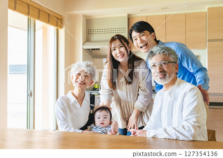 A group photo of a three-generation family happily gathered around a baby in a room 127354136