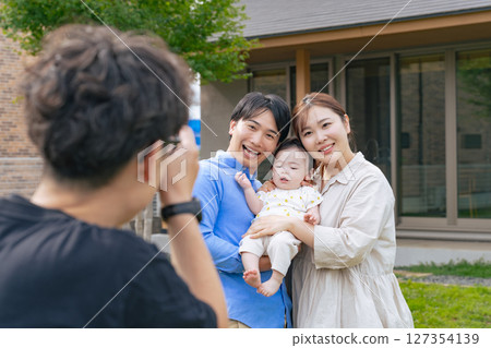 Photographer taking pictures of a parent and baby in front of a house Photographer taking pictures of a parent and baby in front of a house 127354139