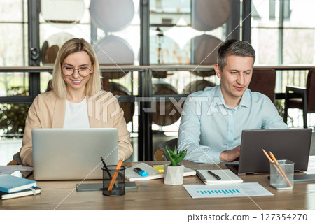 Colleagues sitting at the table in the office and discussing project details Colleagues sitting at the table in the office and discussing project details 127354270