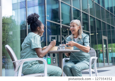 Female doctors having lunch together and looking involved while talking Female doctors having lunch together and looking involved while talking 127354352