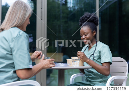 Female doctors having lunch together and looking involved while talking Female doctors having lunch together and looking involved while talking 127354359