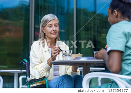 Nurse and a patient on a wheelchair having lunch together and talking Nurse and a patient on a wheelchair having lunch together and talking 127354377