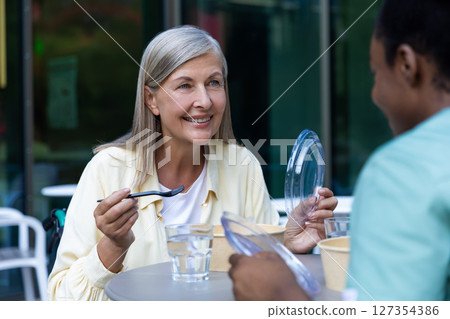 Nurse and a patient on a wheelchair having lunch together and talking 127354386