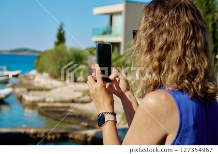 Woman taking photo with smartphone near sea Woman taking photo with smartphone near sea 127354967