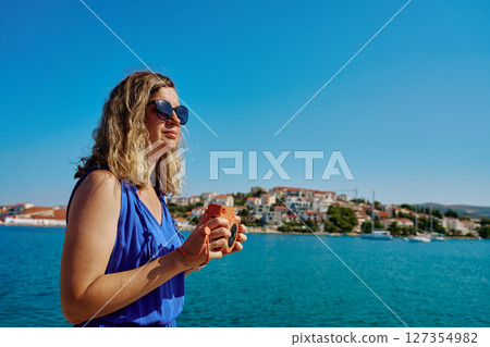 Woman taking photo with instant camera near sea and coastal town 127354982