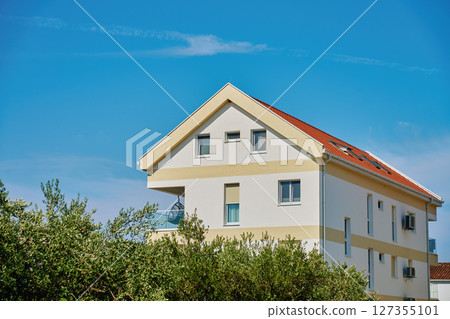 Residential building facade with windows and terrace against blue sky 127355101