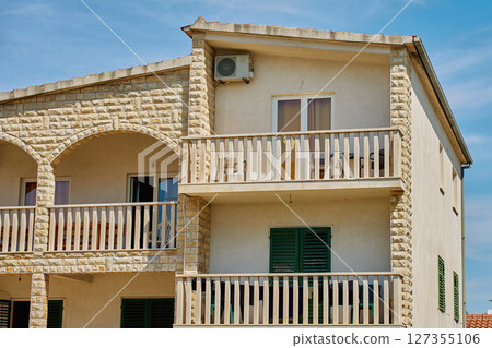 Stone facade house with balconies and shutters under blue sky Stone facade house with balconies and shutters under blue sky 127355106