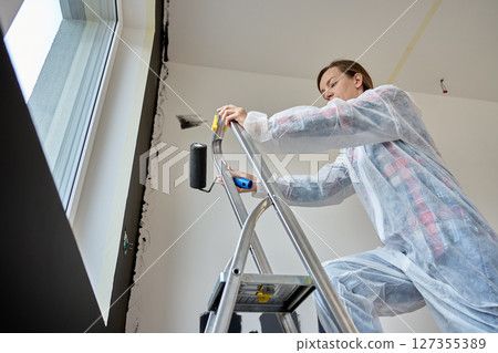 Woman preparing to paint interior wall during apartment renovation Woman preparing to paint interior wall during apartment renovation 127355389