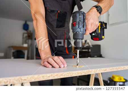Man Drilling Wood Panel with Power Drill in Home Workshop 127355547