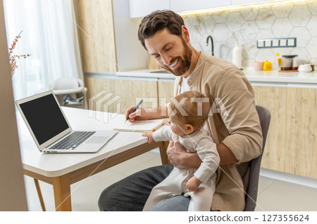 Self-employed young man working from home office while talking care of a baby 127355624