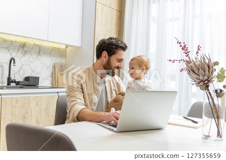 Bearded young caucasian man working from home while taking care of his little son Bearded young caucasian man working from home while taking care of his little son 127355659