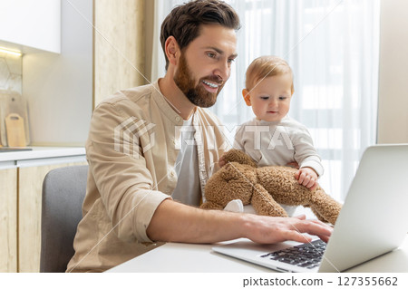 Young bearded man having a video call and holding his little son Young bearded man having a video call and holding his little son 127355662